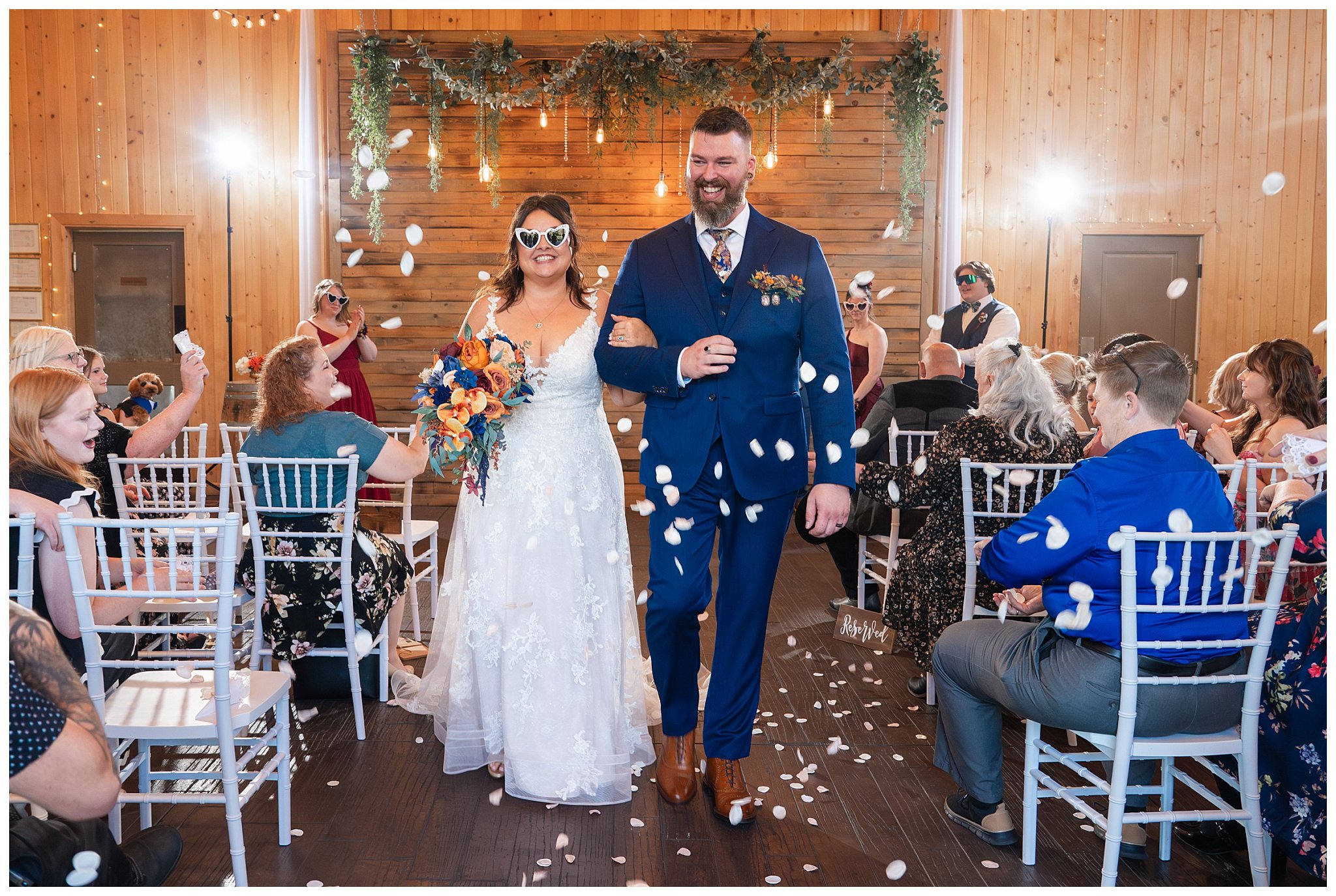 Bride and groom recessional with flower petals being tossed, and wearing sunglasses at the end of ceremony inside the barn at Oak Hills | Star Wars Themed Wedding at Oak Hills Utah | Jessie and Dallin Photography