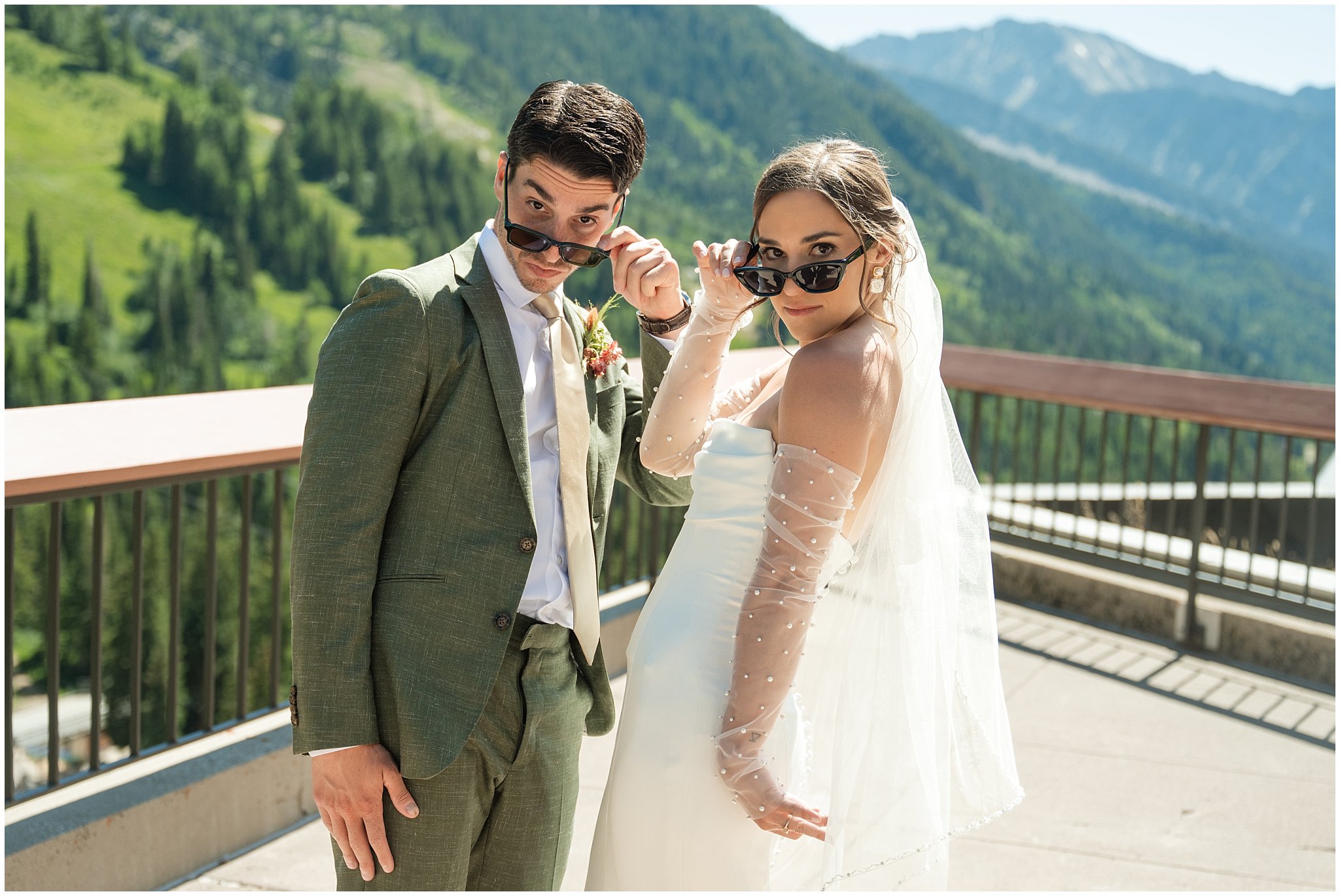 Bride and groom share a moment in sunglasses on the rooftop of The Cliff Lodge. Groom wearing a sage green suit and golden tie, bride in a strapless dress with gloves and veil | Snowbird Summit Summer Wedding | Jessie and Dallin Photography