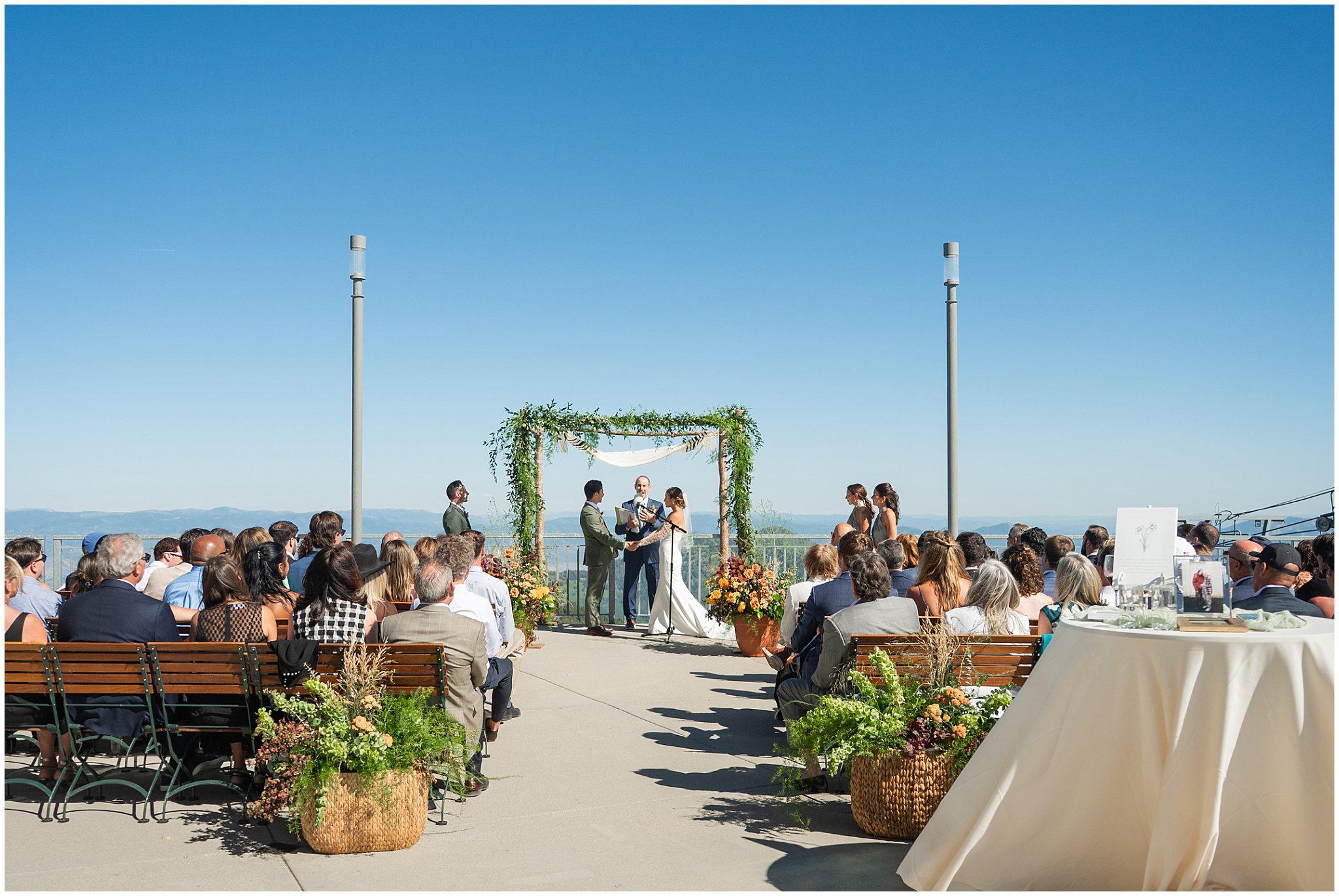 Ceremony site photo. Greenery and florals for the arch surrounded by guests. Groom wearing a sage green suit and golden tie, bride in a strapless dress with gloves and veil | Snowbird Summit Summer Wedding | Jessie and Dallin Photography