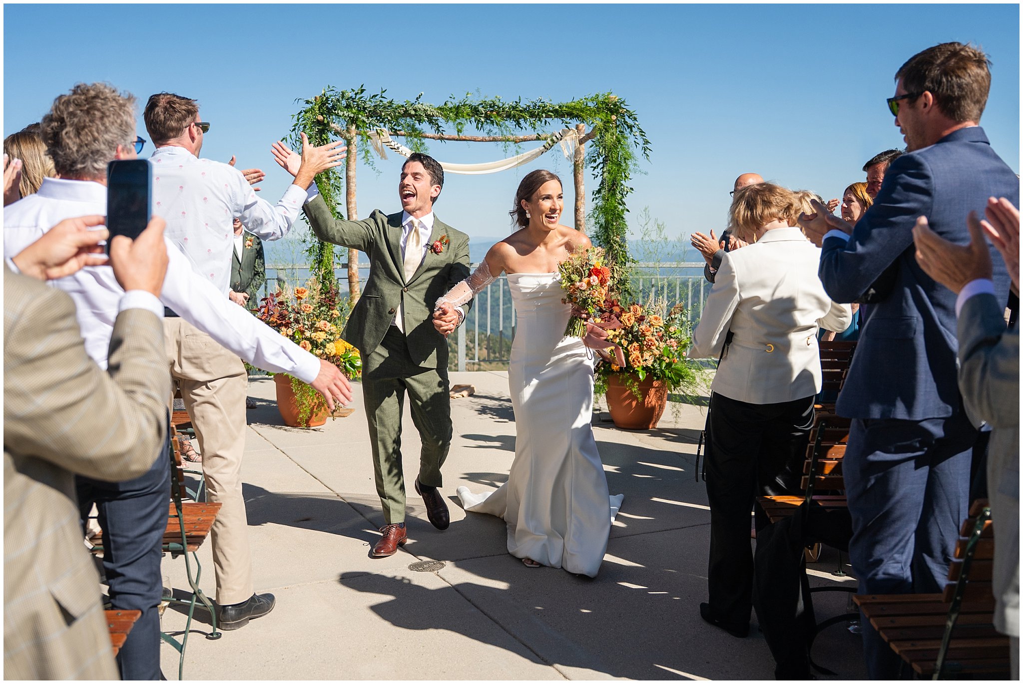 Bride and groom celebrate after ceremony as they walk back down the aisle with their guests. Groom wearing a sage green suit and golden tie, bride in a strapless dress with gloves and veil | Snowbird Summit Summer Wedding | Jessie and Dallin Photography