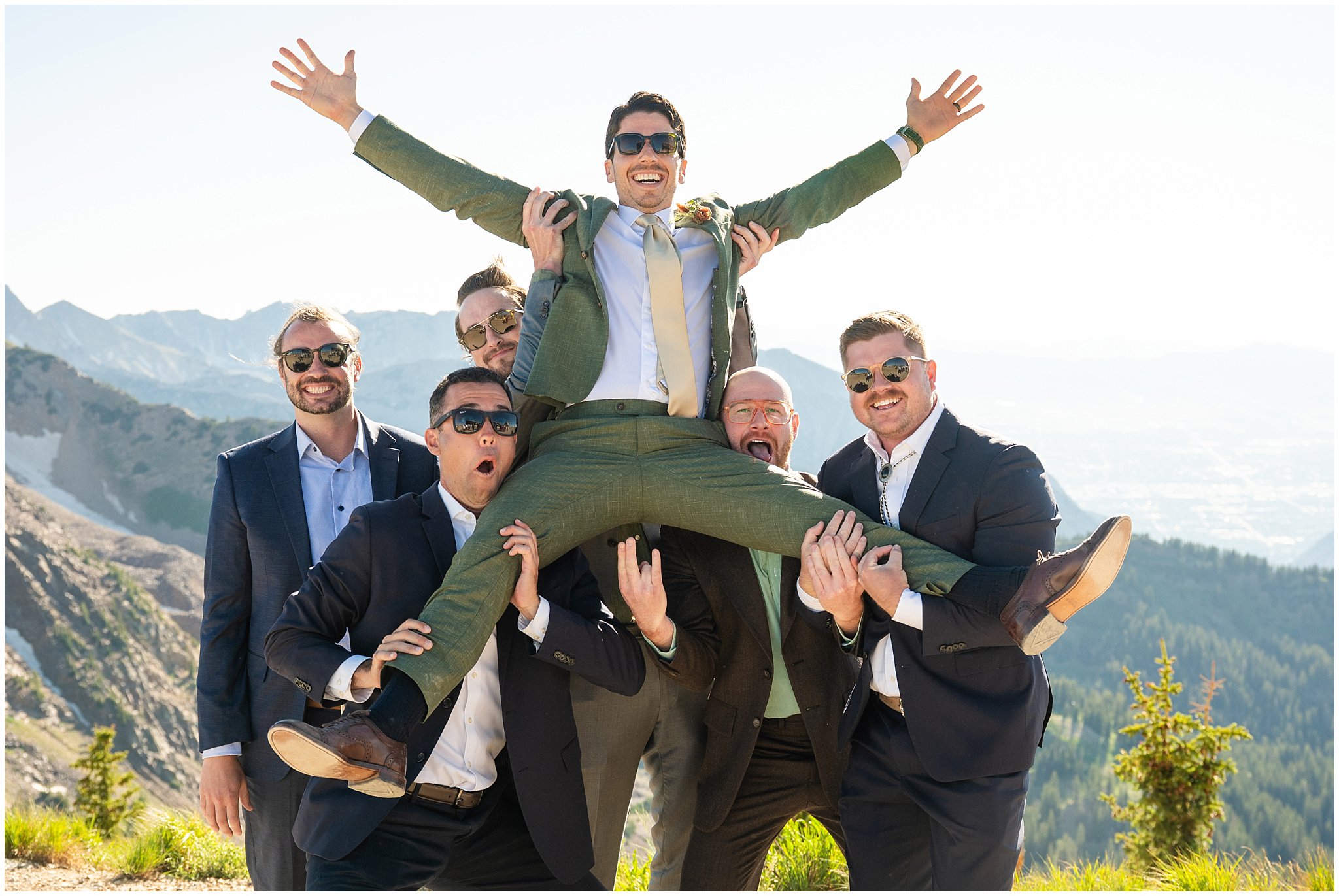 Groom is tossed high in the air by his friends on top of the mountain. Groom wearing a sage green suit and golden tie. | Snowbird Summit Summer Wedding | Jessie and Dallin Photography