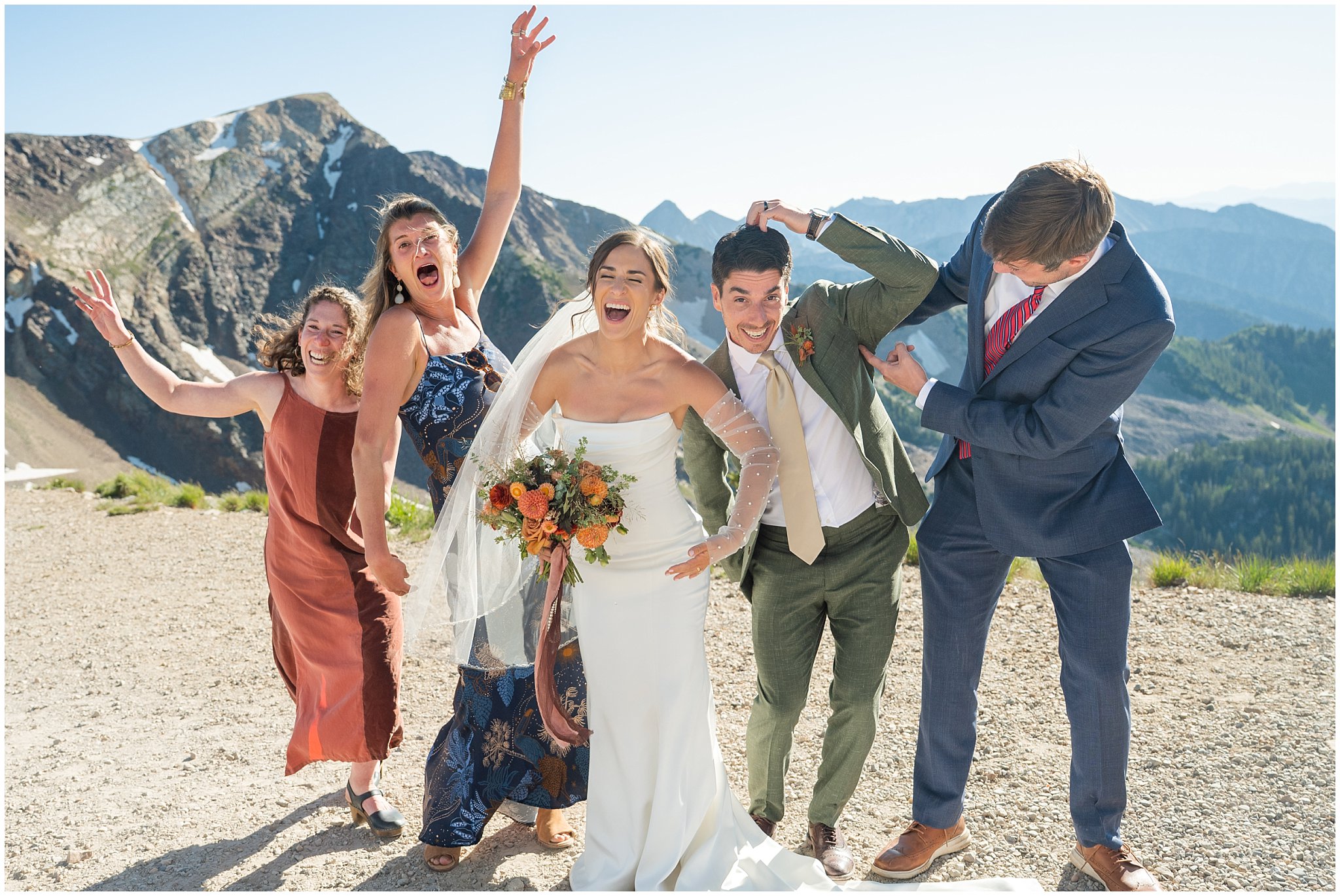 Bride and groom do funny poses with friends on top of the mountain. Groom wearing a sage green suit and golden tie, bride in a strapless dress with gloves and veil | Snowbird Summit Summer Wedding | Jessie and Dallin Photography