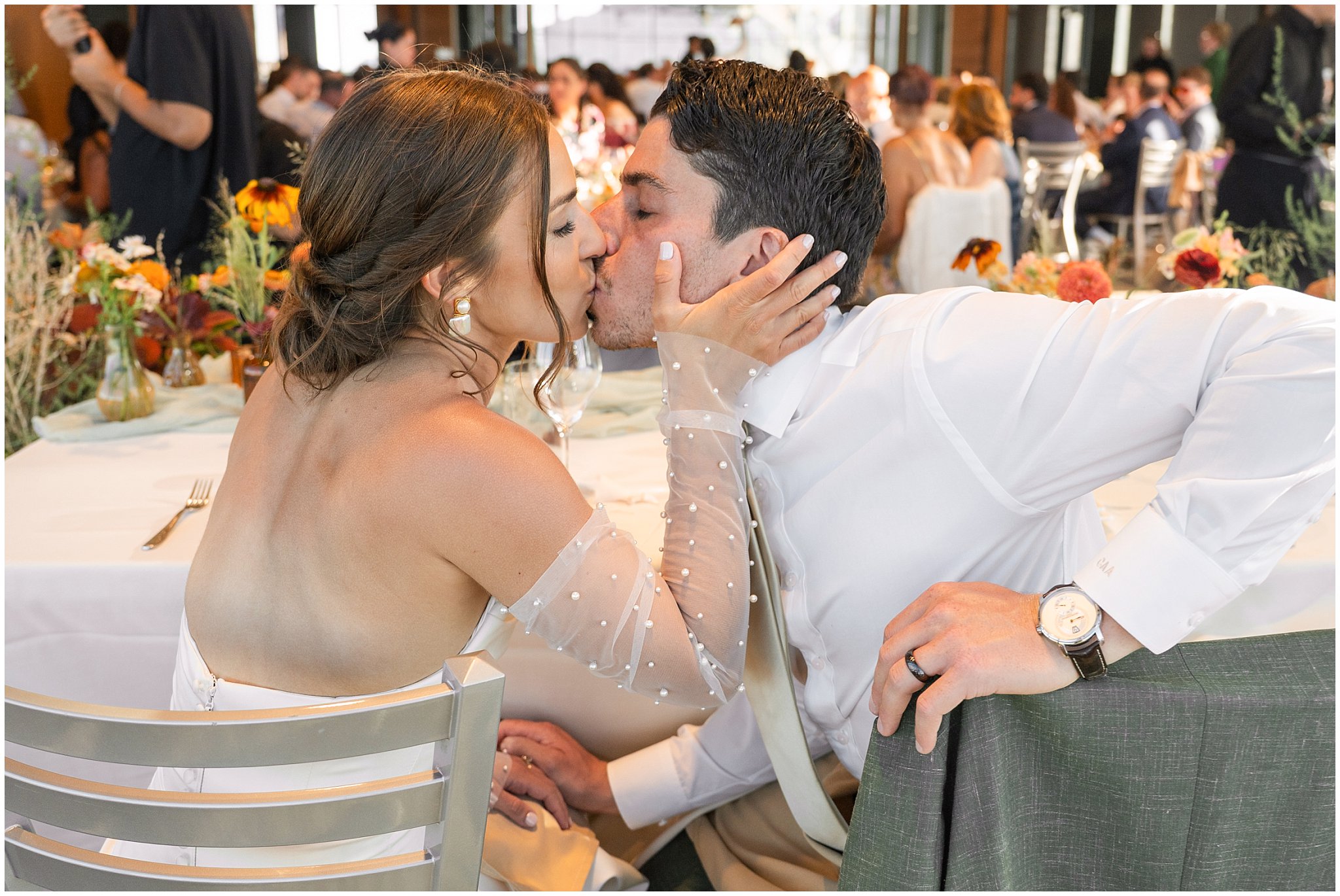 Bride and groom share a kiss at their sweetheart table. Groom wearing a sage green suit and golden tie, bride in a strapless dress with gloves and veil | Snowbird Summit Summer Wedding | Jessie and Dallin Photography