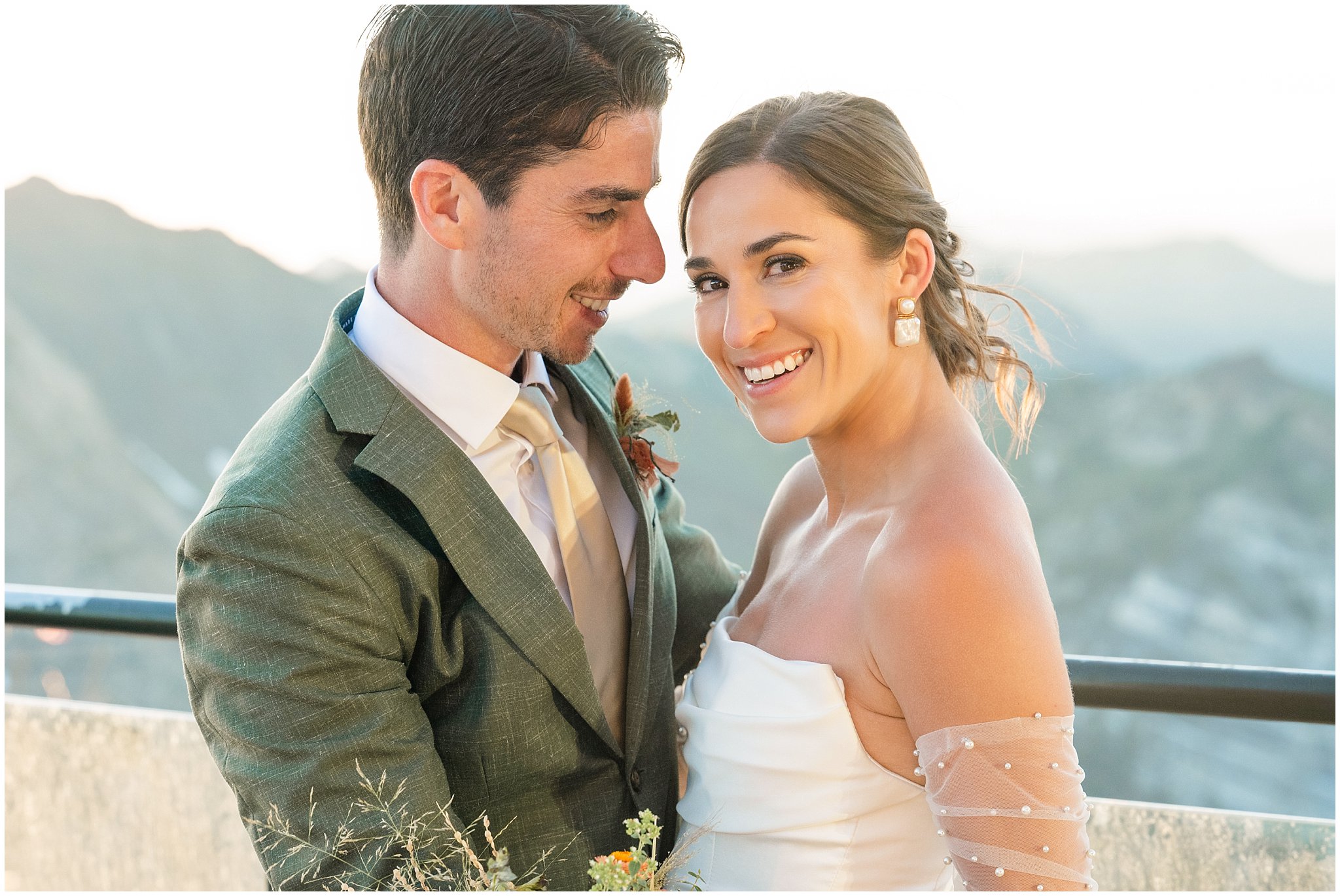 The bride and groom share moments together surrounded by the mountain peaks. Groom wearing a sage green suit and golden tie, bride in a strapless dress with gloves and veil | Snowbird Summit Summer Wedding | Jessie and Dallin Photography