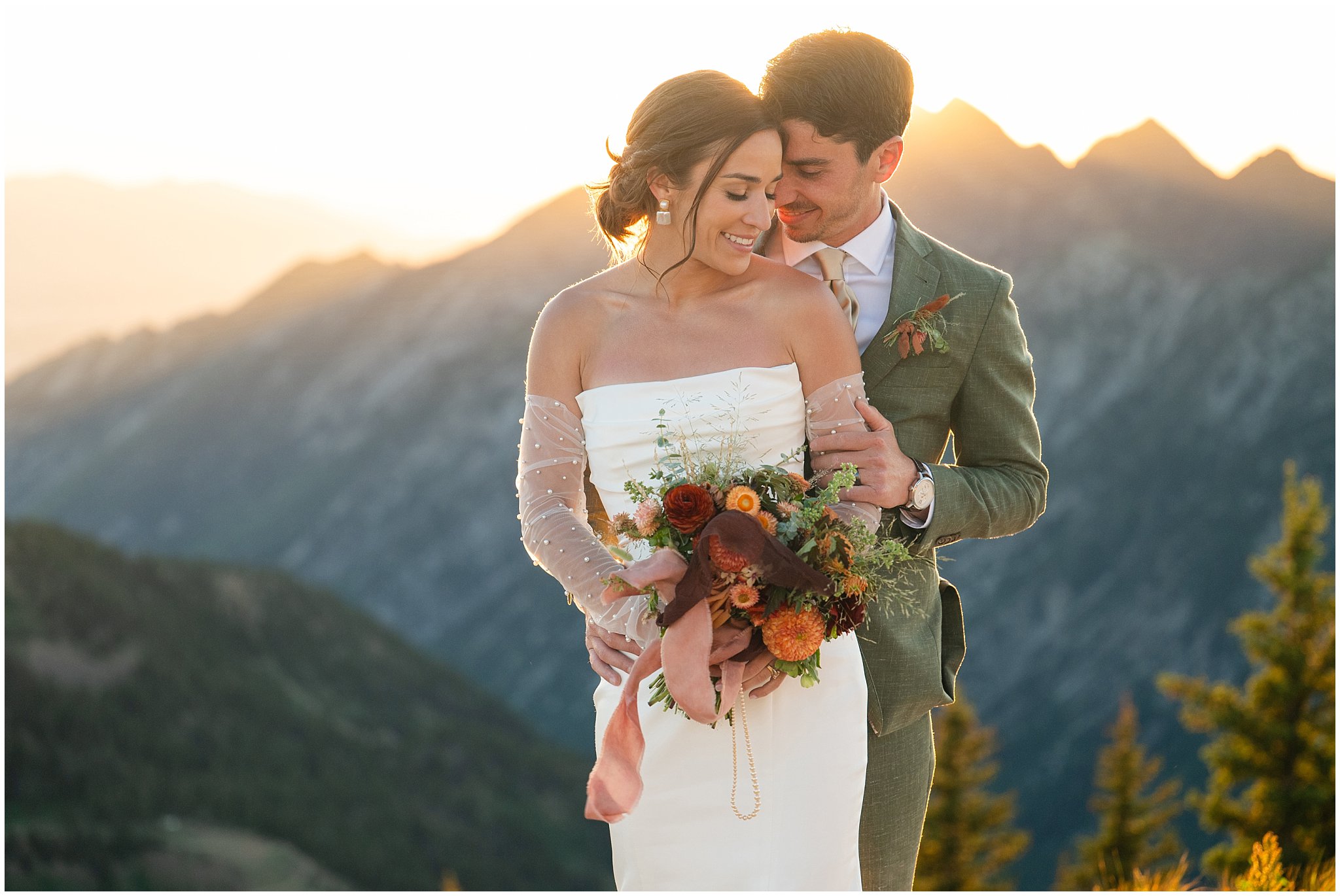 The bride and groom share moments together surrounded by the mountain peaks. Groom wearing a sage green suit and golden tie, bride in a strapless dress with gloves and veil | Snowbird Summit Summer Wedding | Jessie and Dallin Photography