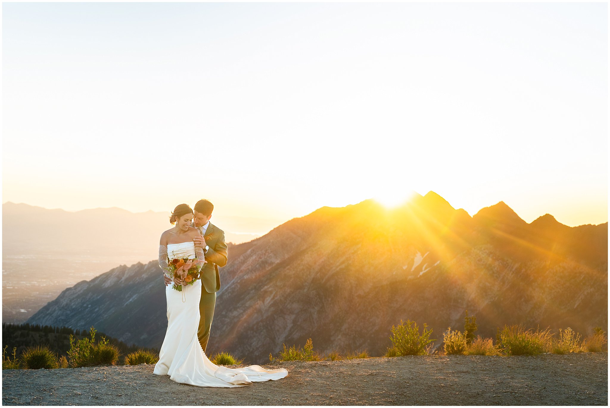 The bride and groom share moments together surrounded by the mountain peaks and a golden sunset and alpen glow. Groom wearing a sage green suit and golden tie, bride in a strapless dress with gloves and veil | Snowbird Summit Summer Wedding | Jessie and Dallin Photography